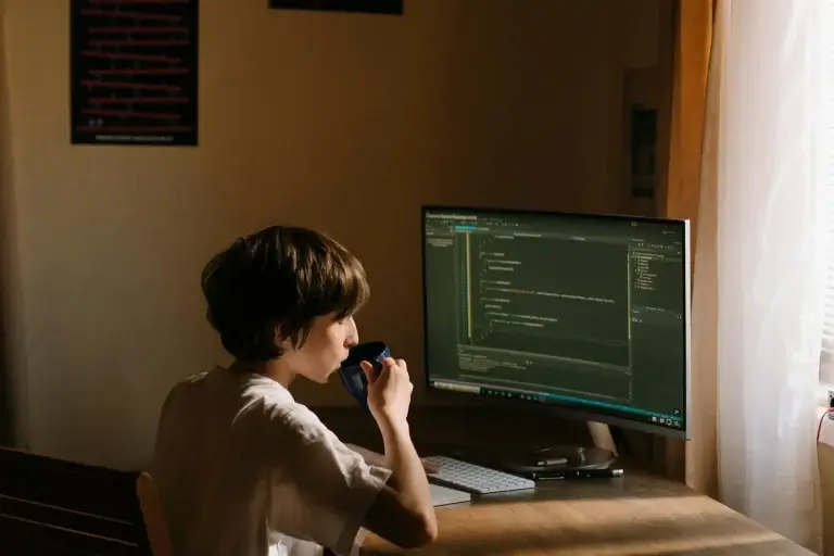 Developer typing prompts to AI coding tool on a laptop in a low-lit workspace
