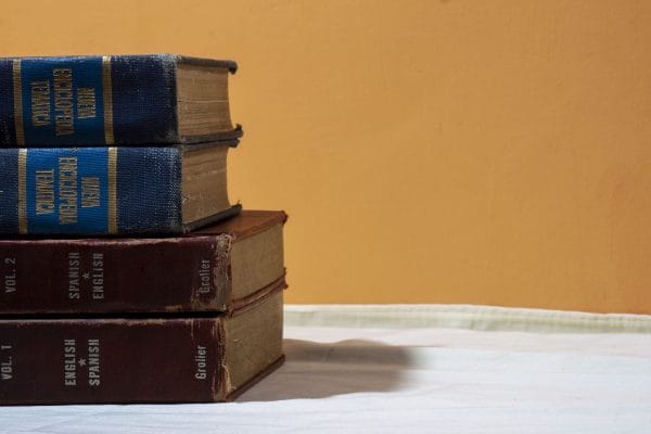 A close-up of vintage English-Spanish dictionaries stacked on a table against a warm backdrop.